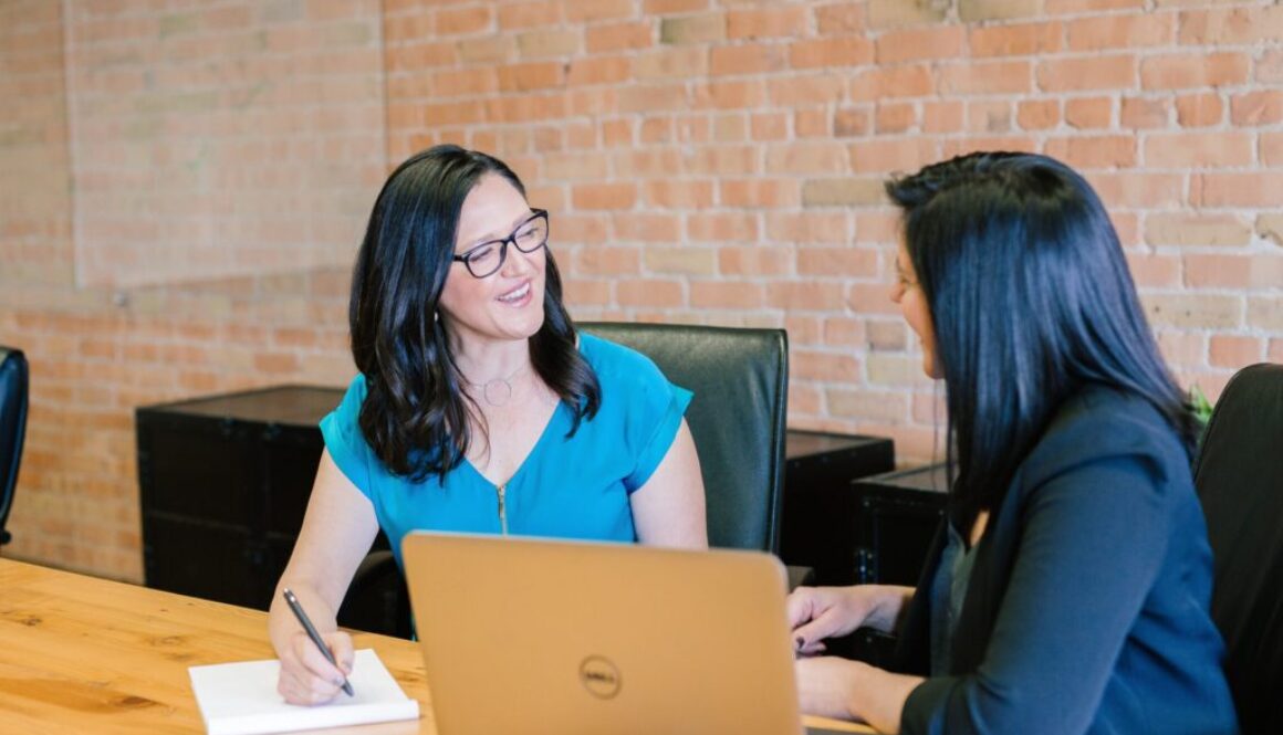 woman in teal t-shirt sitting beside woman in suit jacket